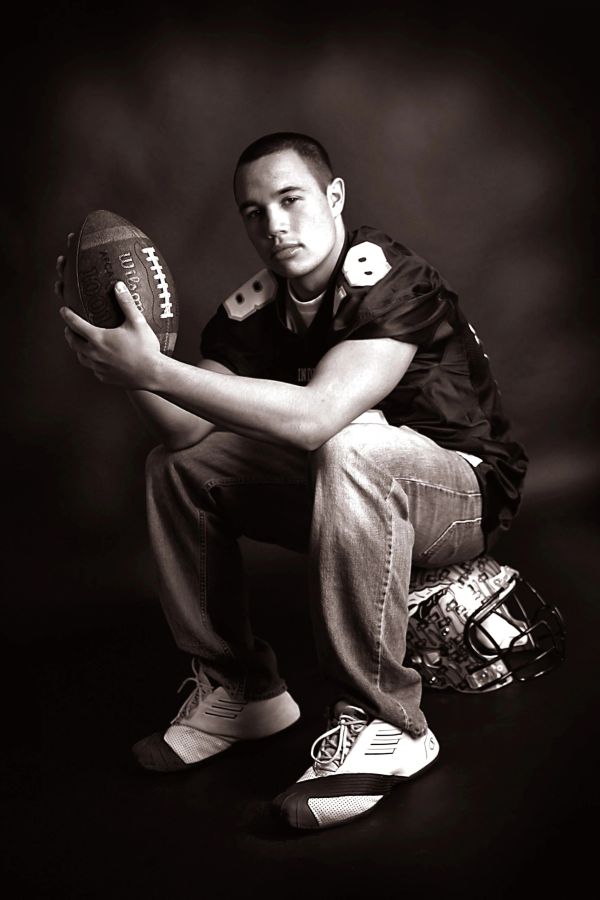 Young football player posing with a ball and helmet in a studio.