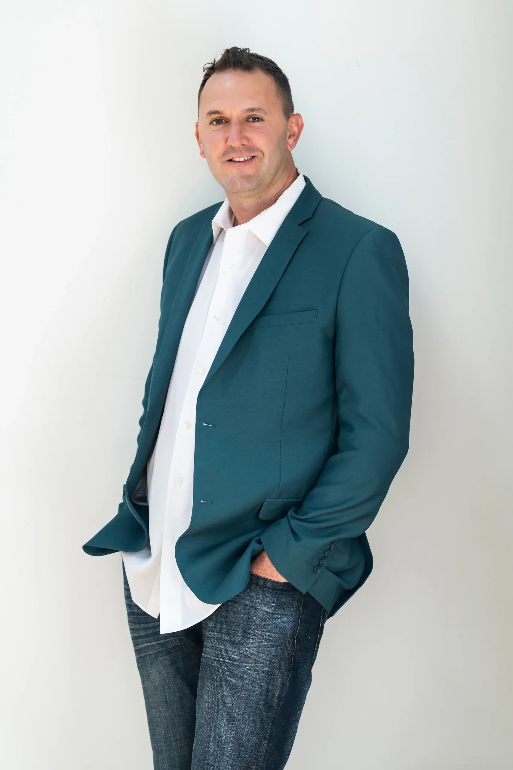 Man in teal blazer and white shirt posing against a plain wall.