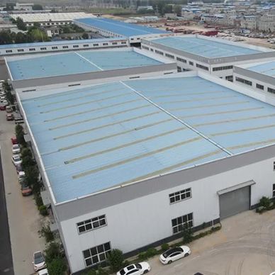 A large industrial warehouse complex with blue roofs and parked cars.
