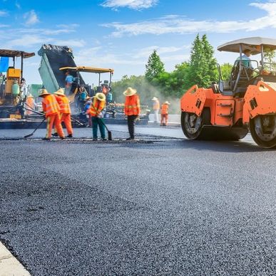 Workers paving a road with heavy machinery under a clear sky.