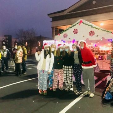 Group in festive pajamas and Santa hats outside decorated building.