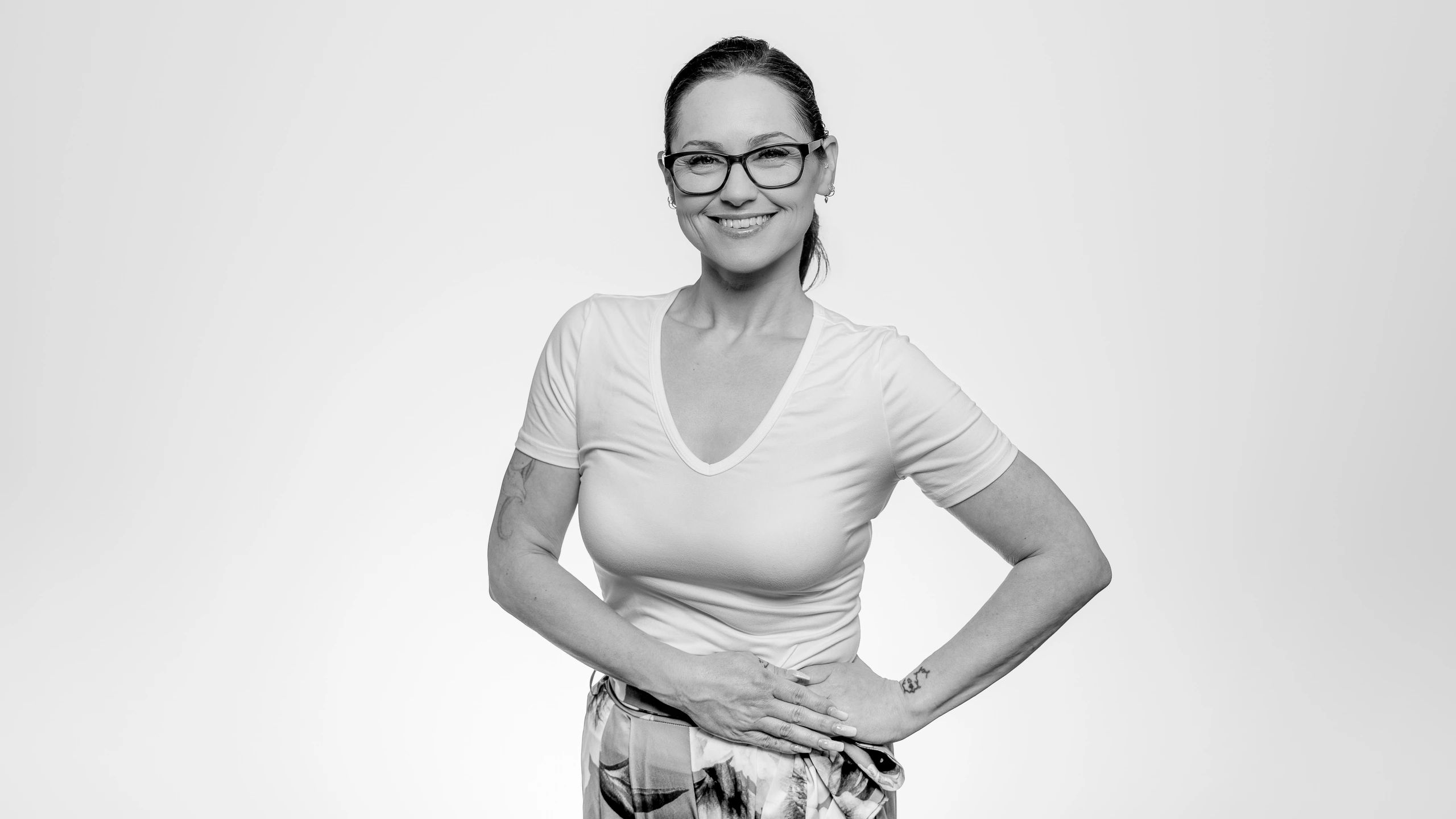 Smiling woman in glasses with tattoos poses confidently.
