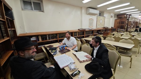 Three men studying religious texts in a library room.