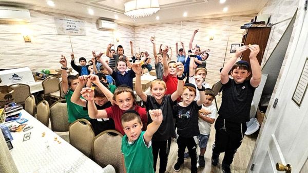 Group of kids raising hands excitedly indoors.