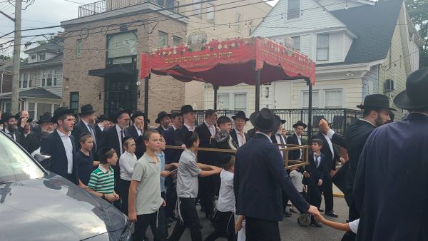 Orthodox Jewish men and boys walking under a canopy in a street procession.