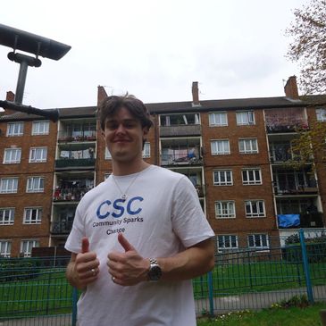 A young man giving thumbs up in front of a residential building.