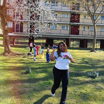 Woman jogging outdoors with children playing in the background on a sunny day.