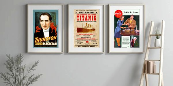 Three vintage posters framed and hung on a gray wall above a shelf and plant.