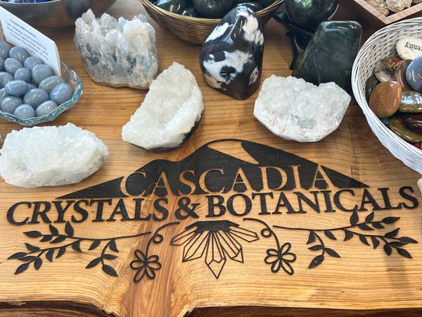 Crystals displayed on a wooden board with Cascadia Crystals &amp; Botanicals logo.