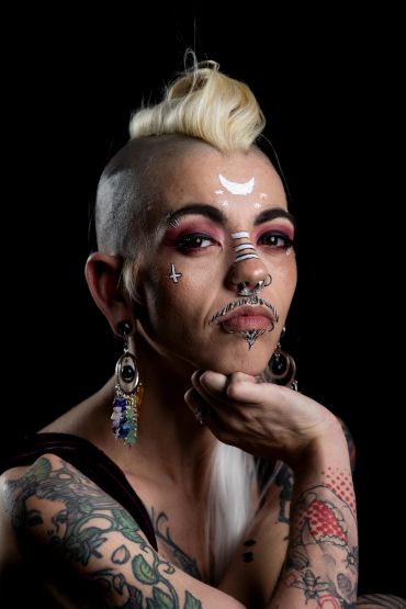 Person with a unique hairstyle, facial piercings, tattoos, and artistic makeup.