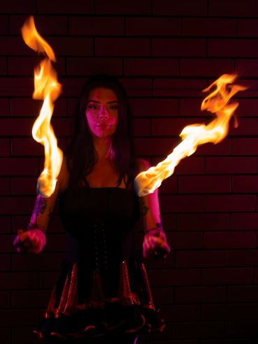 Woman performs fire juggling with intense flames against a brick wall.