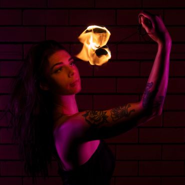 Woman with tattoos holding and playing with fire in dark setting.