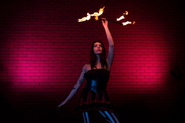 A woman performs fire dancing against a red-lit brick wall.