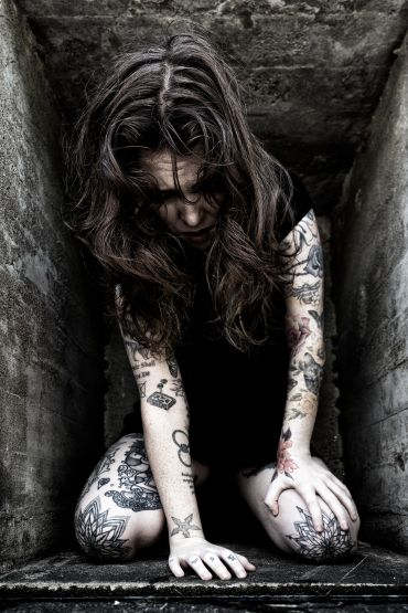 Woman with tattoos kneeling in a dark confined space.