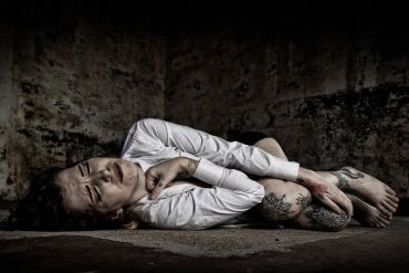Person curled up on the ground looking distressed.