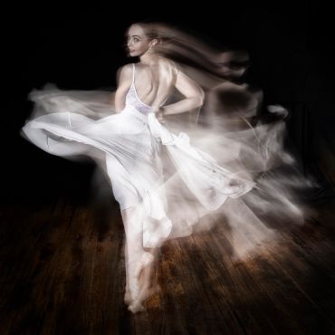 A dancer in a flowing white dress spinning gracefully, captured with motion blur.