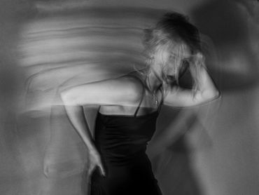 Blurred black-and-white photo of a woman in motion with a hand on her head.