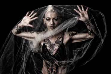 Tattooed woman with a sheer veil against black background.