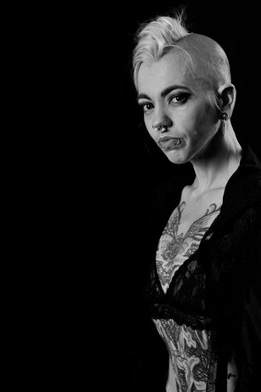 Black and white portrait of a tattooed woman with a mohawk and piercings.