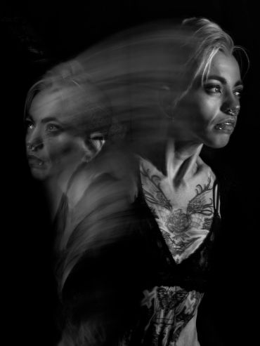 Black and white portrait with motion blur effect showing a tattooed woman.