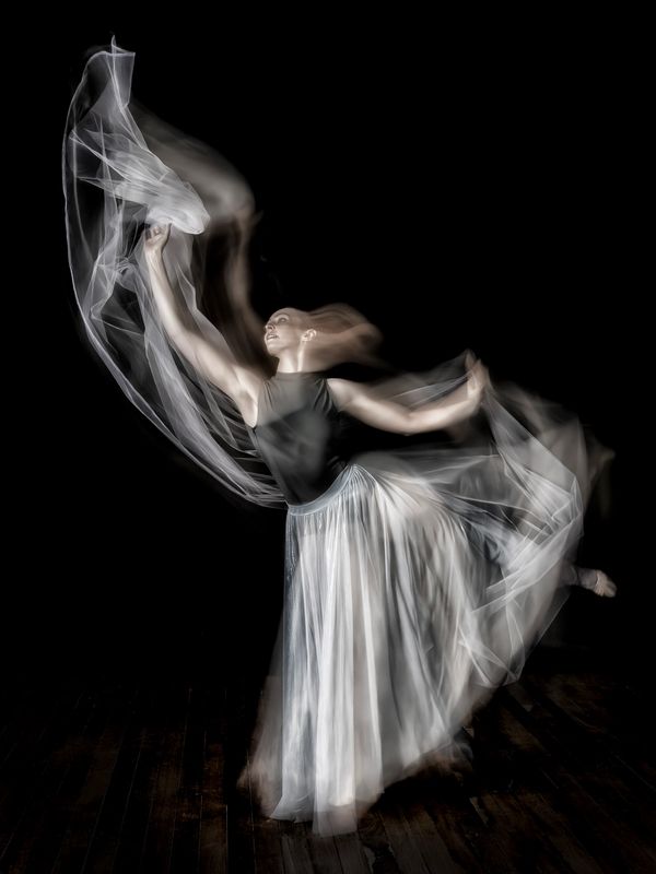 A graceful dancer in motion with flowing fabric on a dark background.
