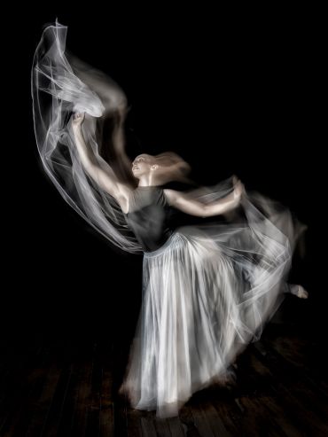 A graceful dancer moves fluidly with flowing fabric in a dynamic pose.