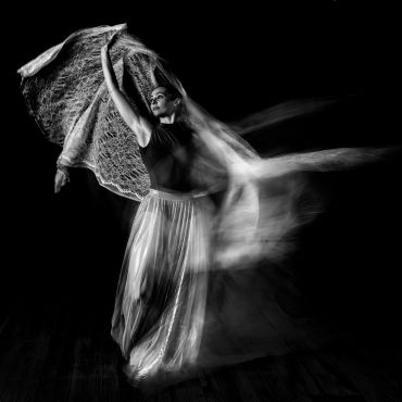 Black and white photo of a dancer with flowing fabric in motion.