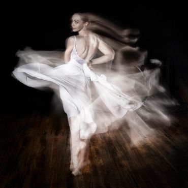 A woman in a white dress twirls gracefully, creating motion blur.