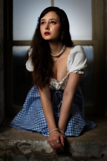 Young woman in vintage dress sitting by a window.