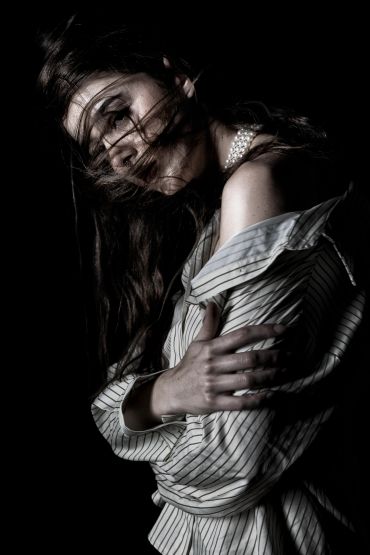 Woman with wind-blown hair in striped shirt and pearls against black background.
