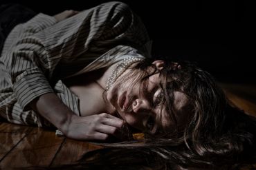A woman lies on a wooden floor in dramatic lighting.