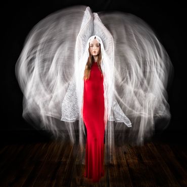 Woman in red gown with ethereal white wings effect against black background.