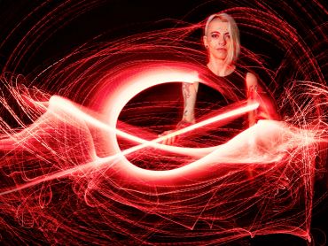 A woman surrounded by dynamic red light trails in a dark setting.