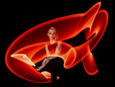 Person with tattoos surrounded by swirling red light trails in dark setting.