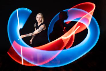 Two women create colorful light trails with glowing sticks in a dark setting.