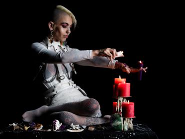 Person performing a ritual with candles and a doll in a dark setting.