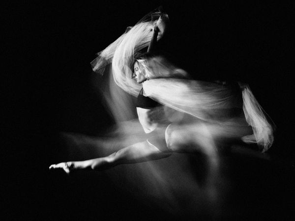 Black and white photo of a dancer leaping with flowing fabric.