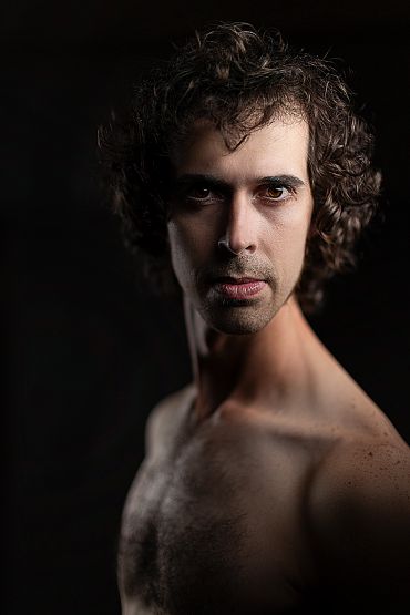 Portrait of a shirtless man with curly hair.