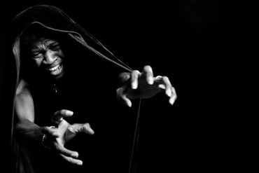 A person with a hood reaches out intensely in black and white.
