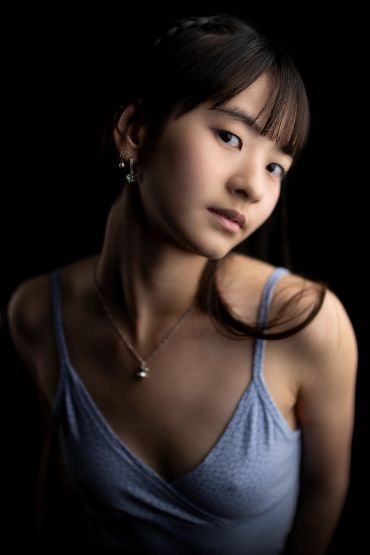Portrait of a young woman in a blue dress with a dark background.