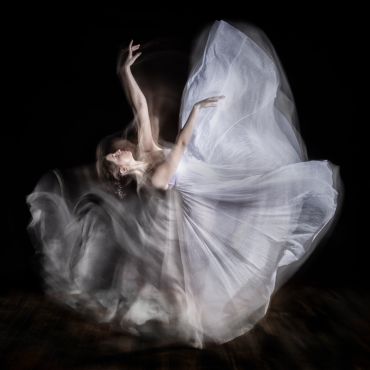 A dancer in a flowing white dress captured in graceful motion against a dark background.
