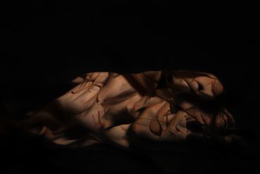 Nude figure artfully lit with shadows and highlights in darkness.