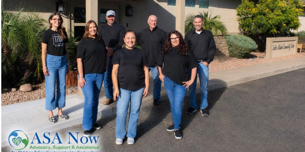 Group of seven people standing outside a community center under sunlight.