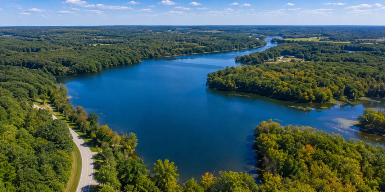 A winding river surrounded by dense green forest under a blue sky.