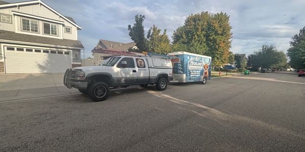 A work truck with a trailer parked on a suburban street under a cloudy sky.