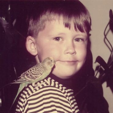 Young boy with a bird perched on his shoulder.