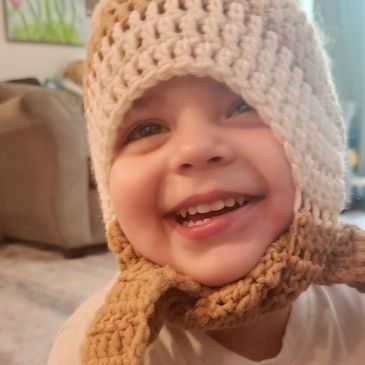 Smiling toddler wearing a cozy crocheted hat indoors.