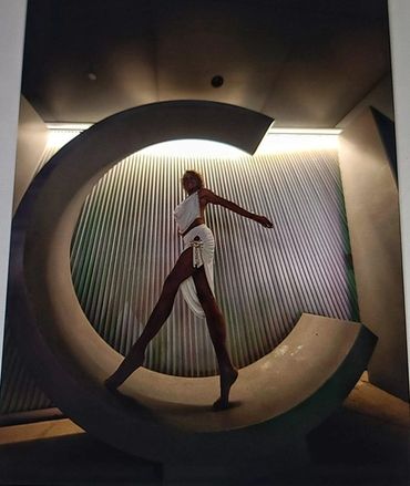 Model posing inside large letter C with artistic lighting.