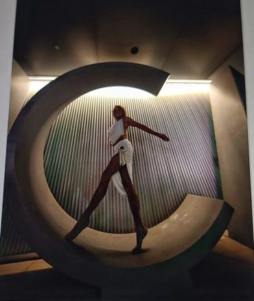 Model posing inside large letter C with artistic lighting.