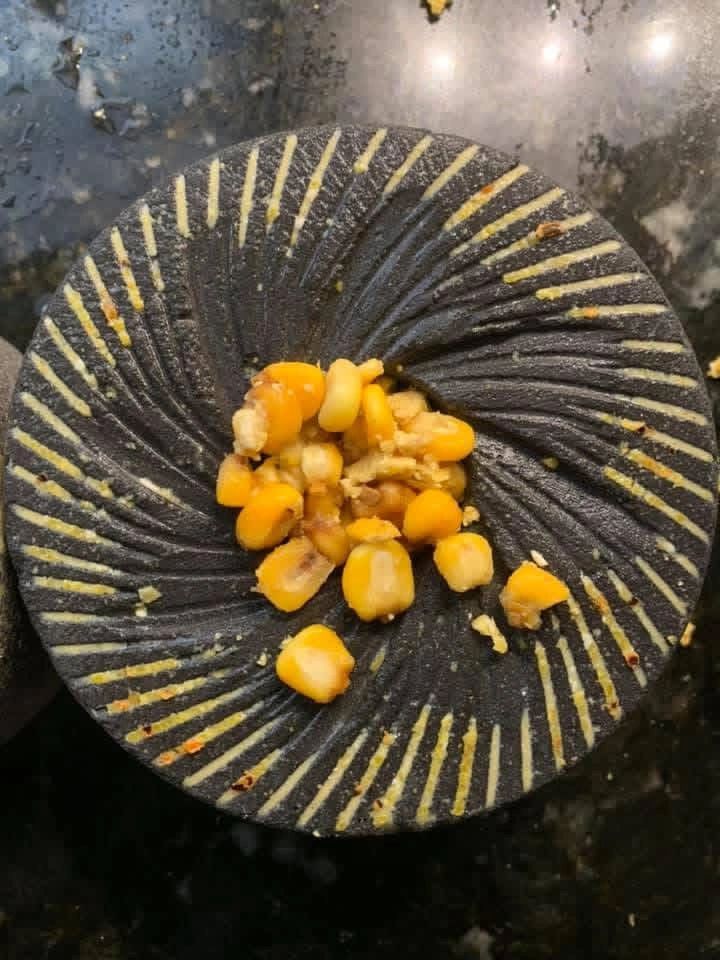 A granite grinding stone with corn kernels on top, used for traditional food preparation.